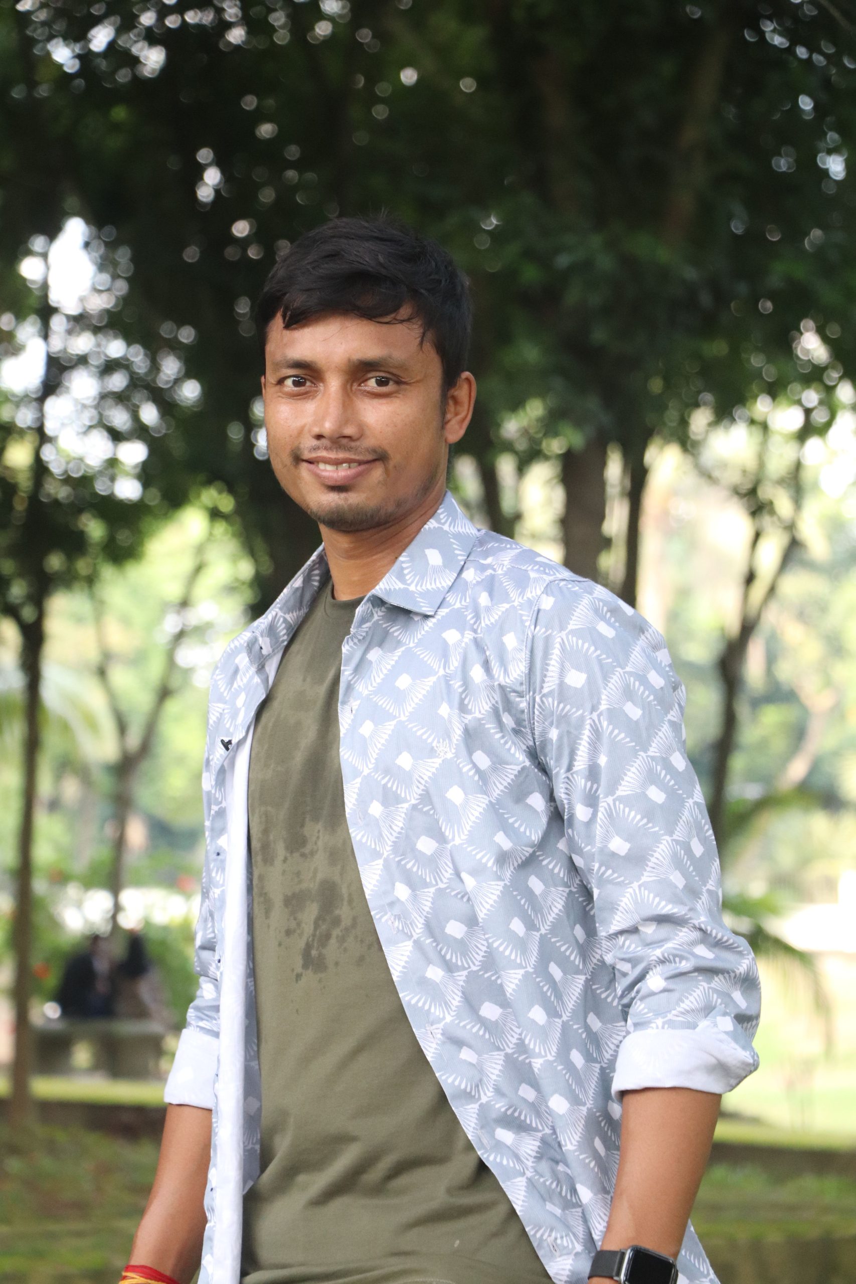 Smiling young man in a casual shirt posing under trees in Rangpur, Bangladesh.