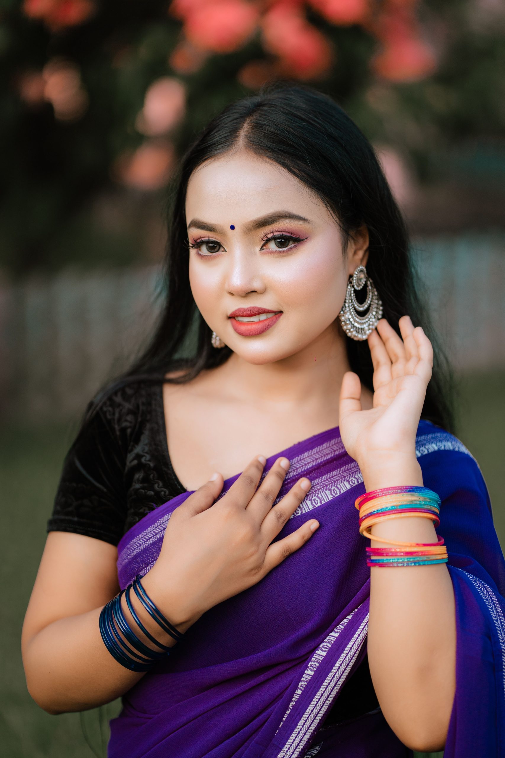 Beautiful South Asian woman in a purple sari and traditional jewelry, smiling outdoors.